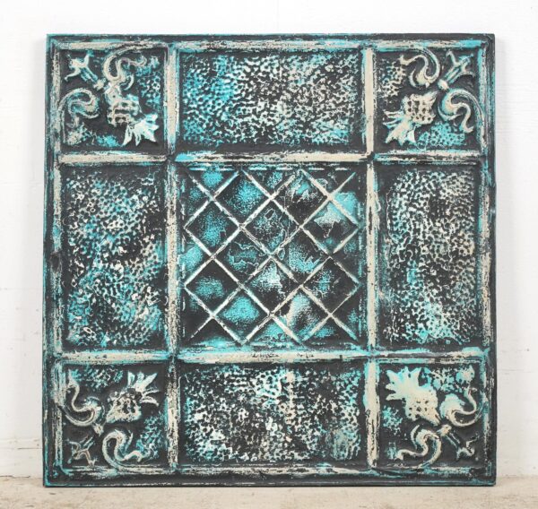 Handcrafted tin wall panel with a grid of textured sections and ornate corner details in black, blue, and white.