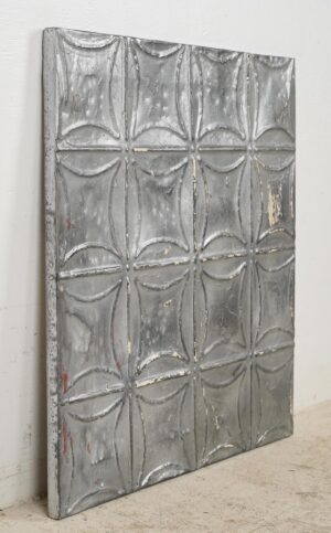 Handcrafted gray tin wall panel with a raised geometric ceiling pattern shown at an angle, featuring worn edges and a weathered surface.